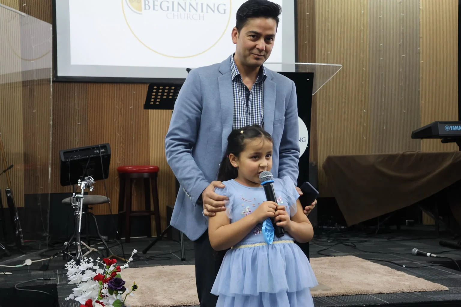 A pastor standing with a young girl as she speaks into the microphone