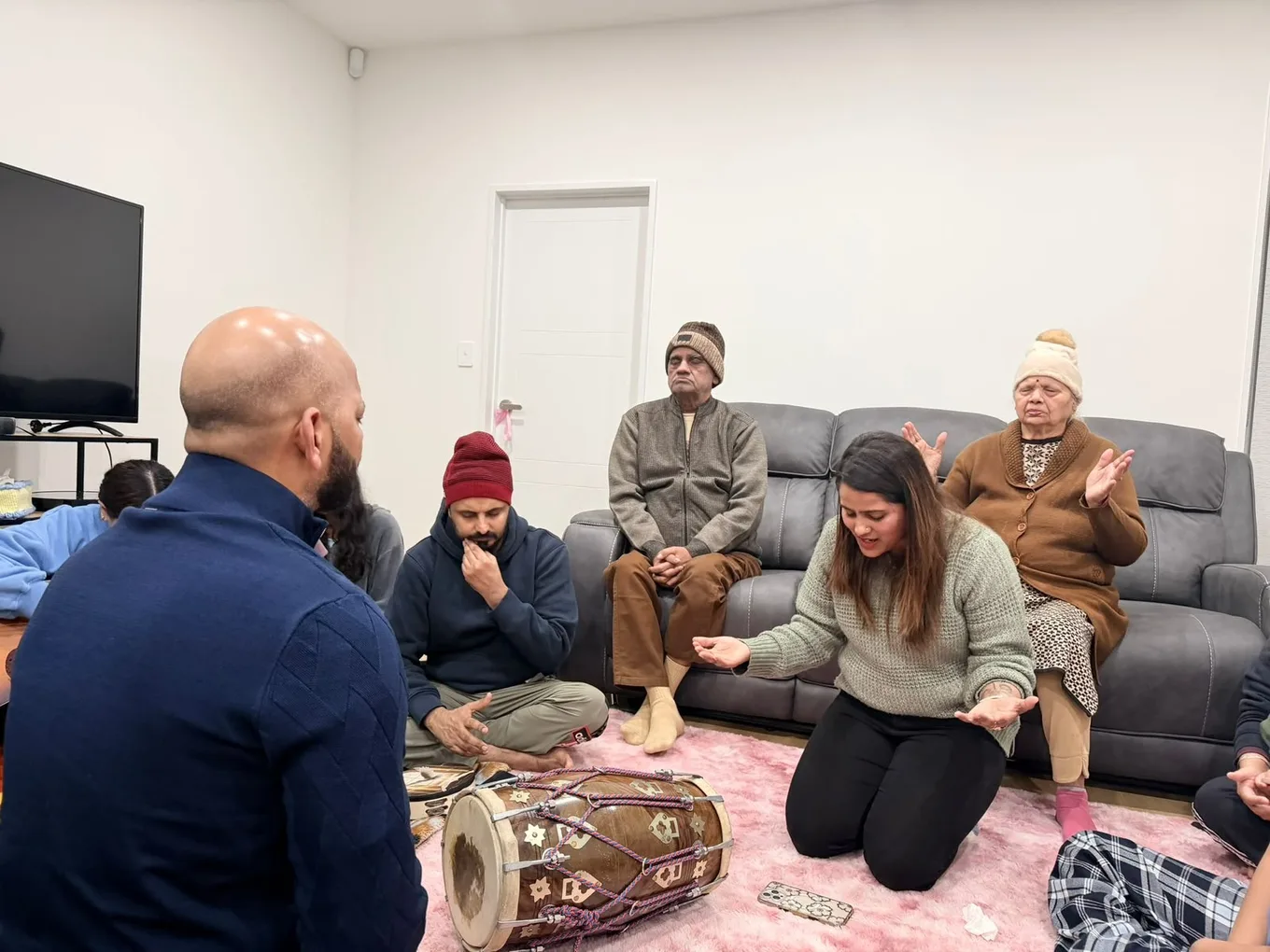Members of the church sitting together on the floor of a home during a midweek gathering, one playing a dholak